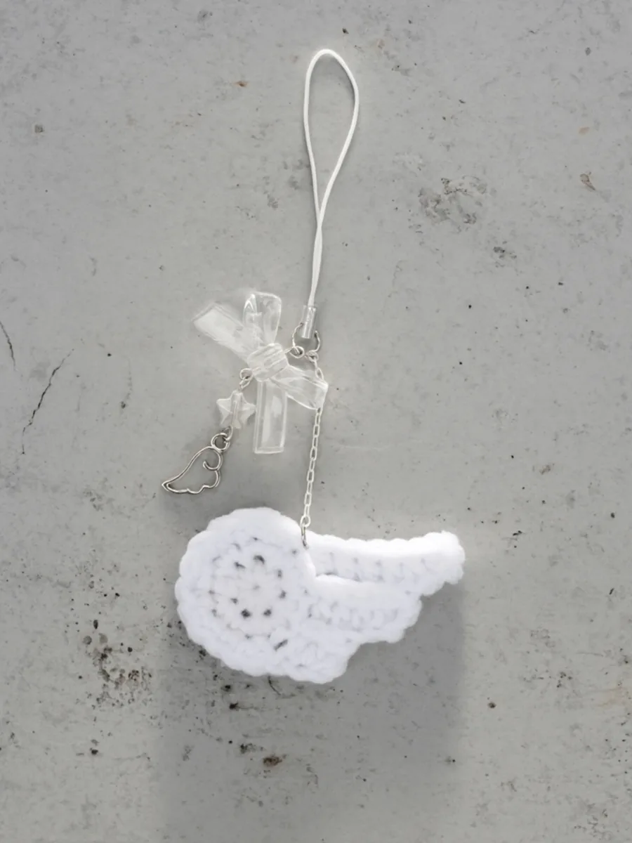 A white crocheted wing charm on a clear ribbon strap, on grey concrete
